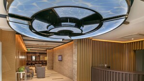 A modern hotel lobby with a curved reception desk, seating area, and a ceiling with a unique geometric design. - B Business Hotel & Spa (Antalya)