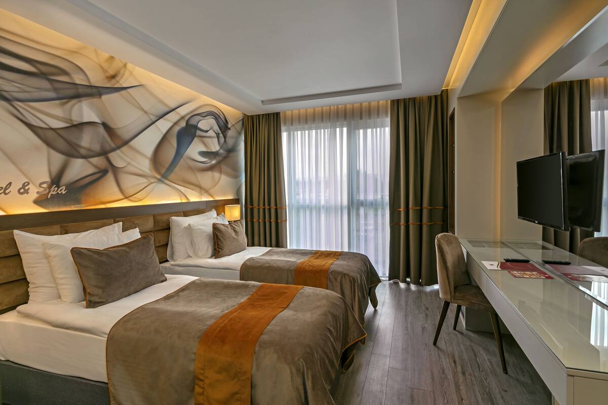 A hotel room with two beds, a desk, a television, and a large abstract wall art piece.