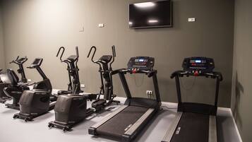 A fitness room with multiple cardio machines, including treadmills and elliptical trainers, arranged in a row.