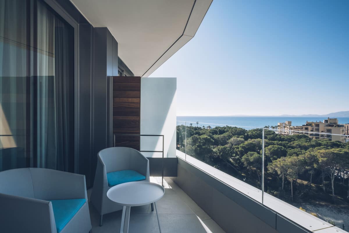 Ein Balkon mit zwei Stühlen und Blick auf das Meer und Bäume.