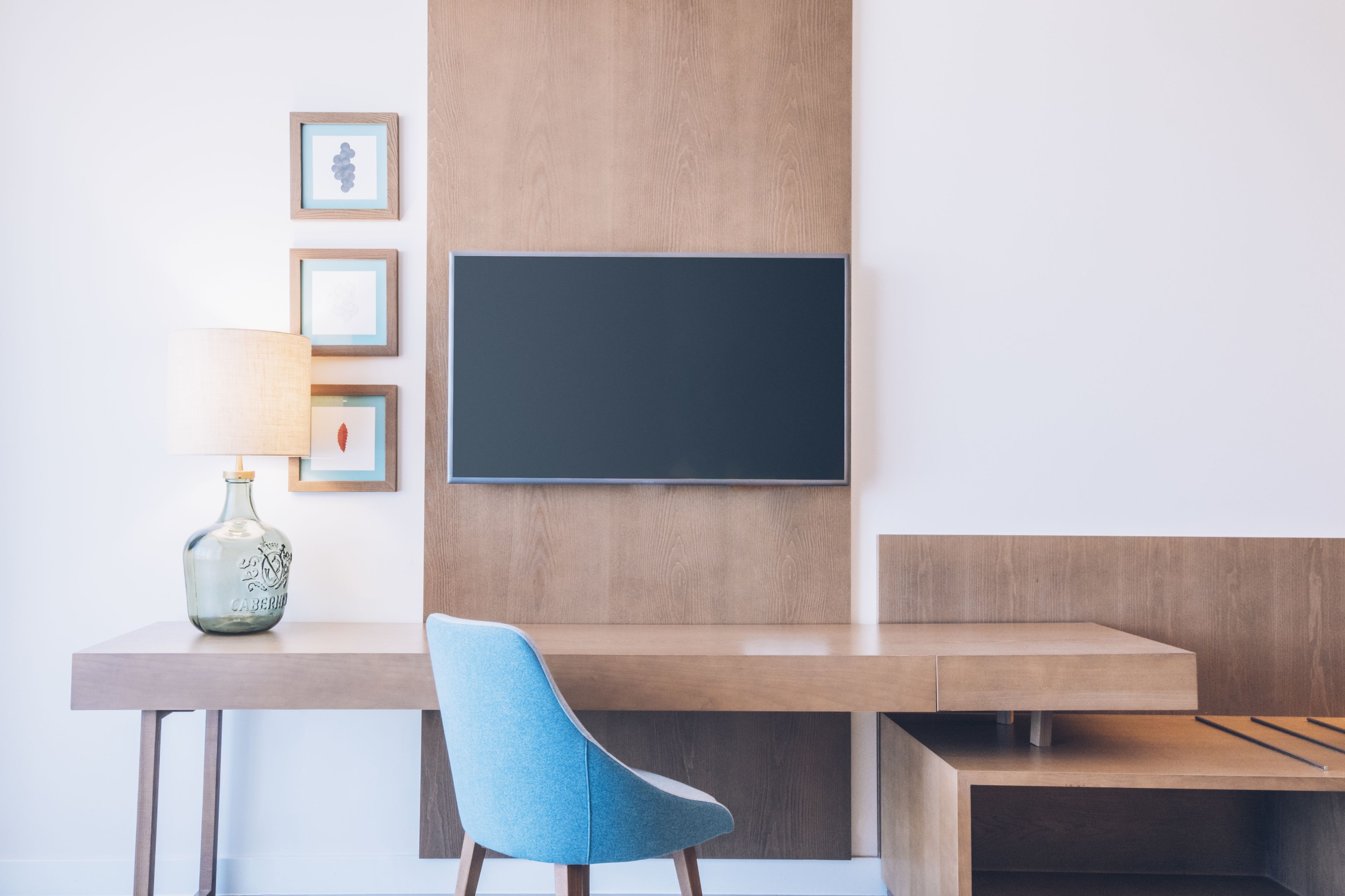 Una habitación moderna con un escritorio de madera, una silla azul, un jarrón y cuadros en la pared.