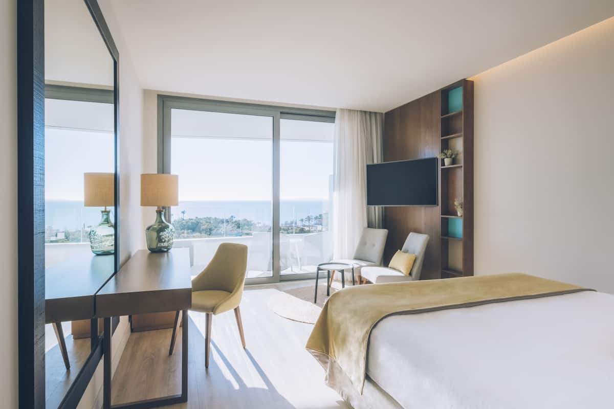 Ein Hotelzimmer mit Bett, Schreibtisch mit Stuhl, Fernseher und Balkon mit Blick.