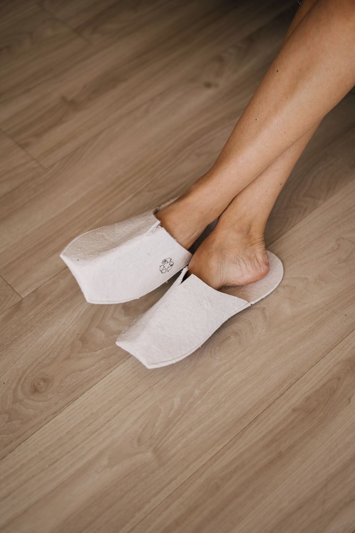 Un par de zapatillas blancas con un símbolo de reciclaje en la suela, sobre un piso de madera.