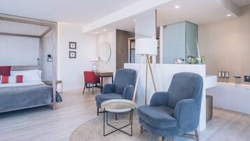 Una habitación de hotel moderna con cama, dos sillones, una mesita, un escritorio y un baño con espejo y lavamanos.