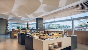 A modern breakfast buffet with a variety of food items, a geometric ceiling design, and large windows offering a view of the outdoors.