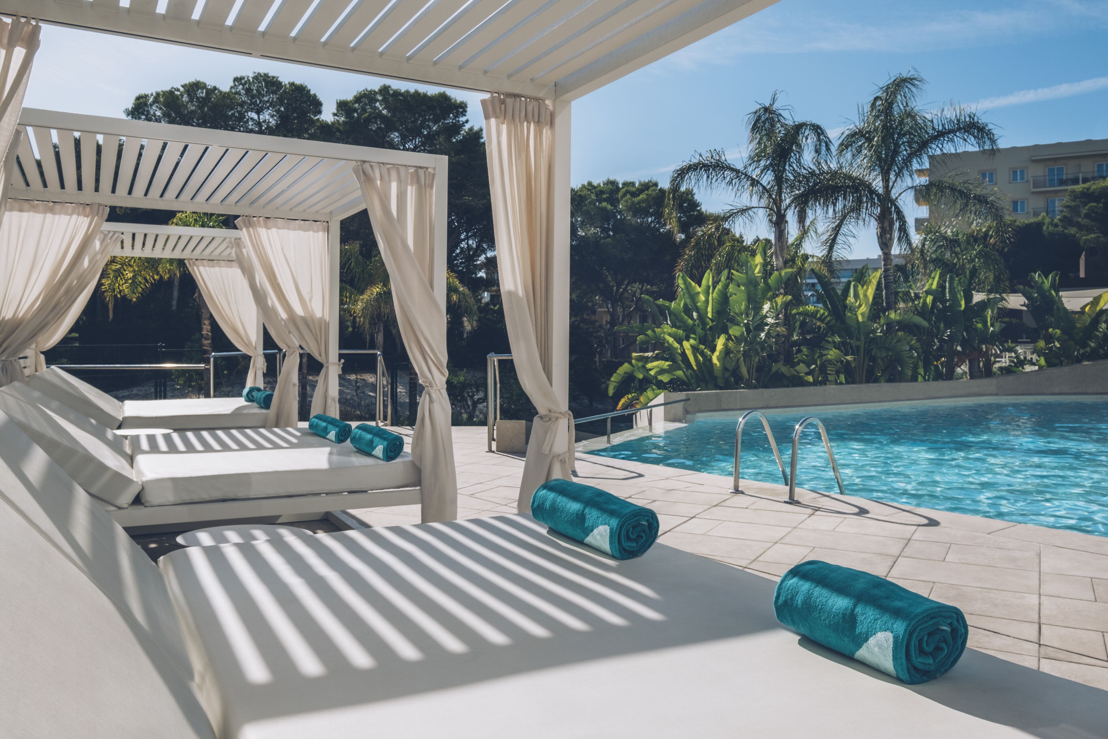 A poolside area with a covered seating area, a pool, and surrounding greenery.