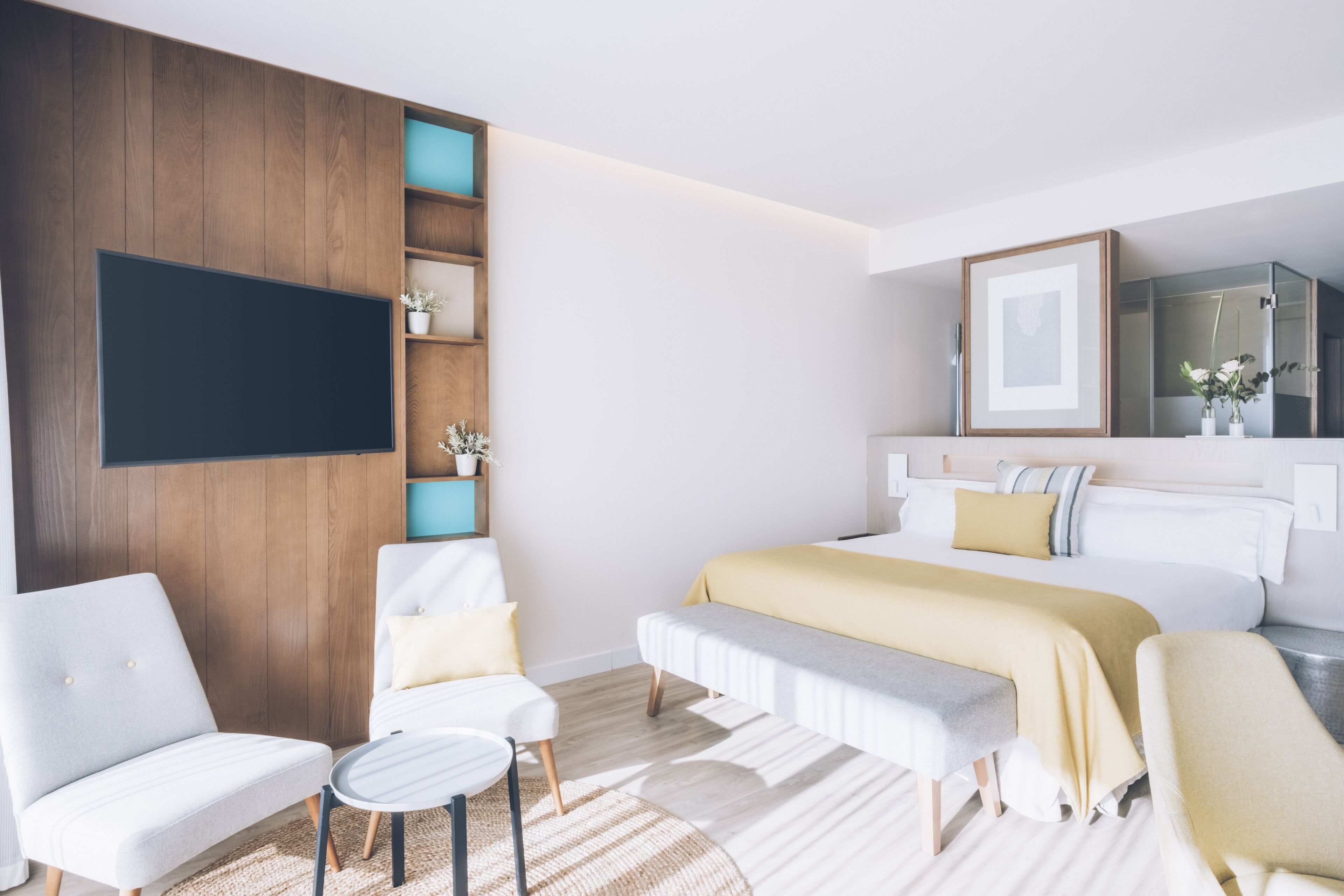 A modern hotel room with a large bed, a sofa, a small table, and a TV mounted on the wall.