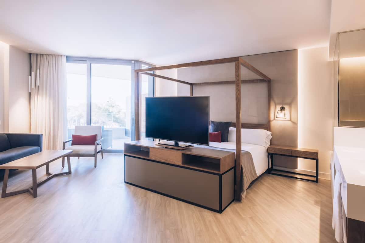 Ein modernes Hotelzimmer mit großem Flachbildfernseher, einem hölzernen Bettgestell, einem Nachttisch, einer Couch und einem großen Fenster mit Blick auf die Stadt.
