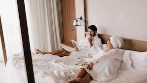 A hotel room with a bed, a bedside table, a lamp, and a window with curtains.