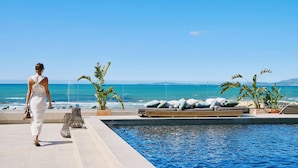 A pool area with a view of the ocean, a woman walking, and seating with plants.