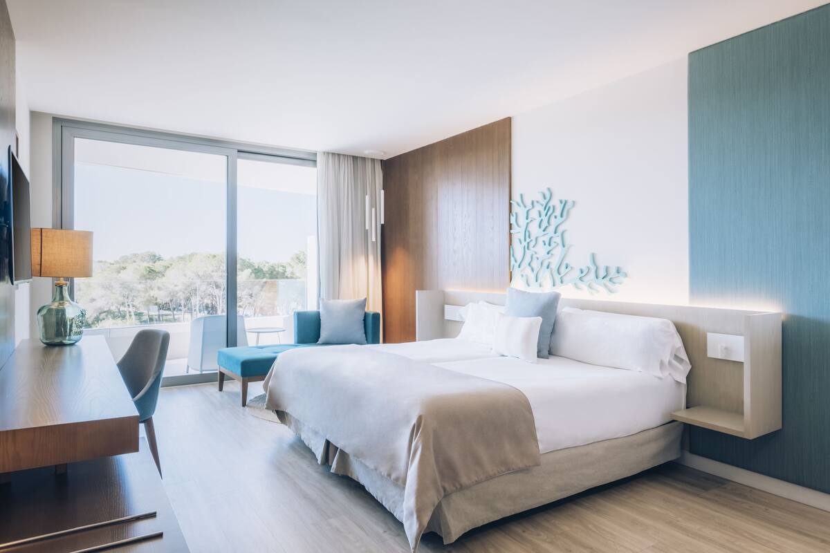 Ein Hotelzimmer mit einem großen Bett, einem Schreibtisch, einem Sessel und Blick ins Freie.