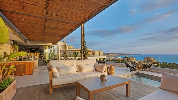 A modern outdoor living area with a wooden deck, a sofa, a coffee table, and a pool.