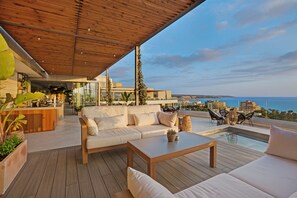 Een moderne buitenruimte met een houten terras, een bank, een bijzettafeltje en een zwembad.