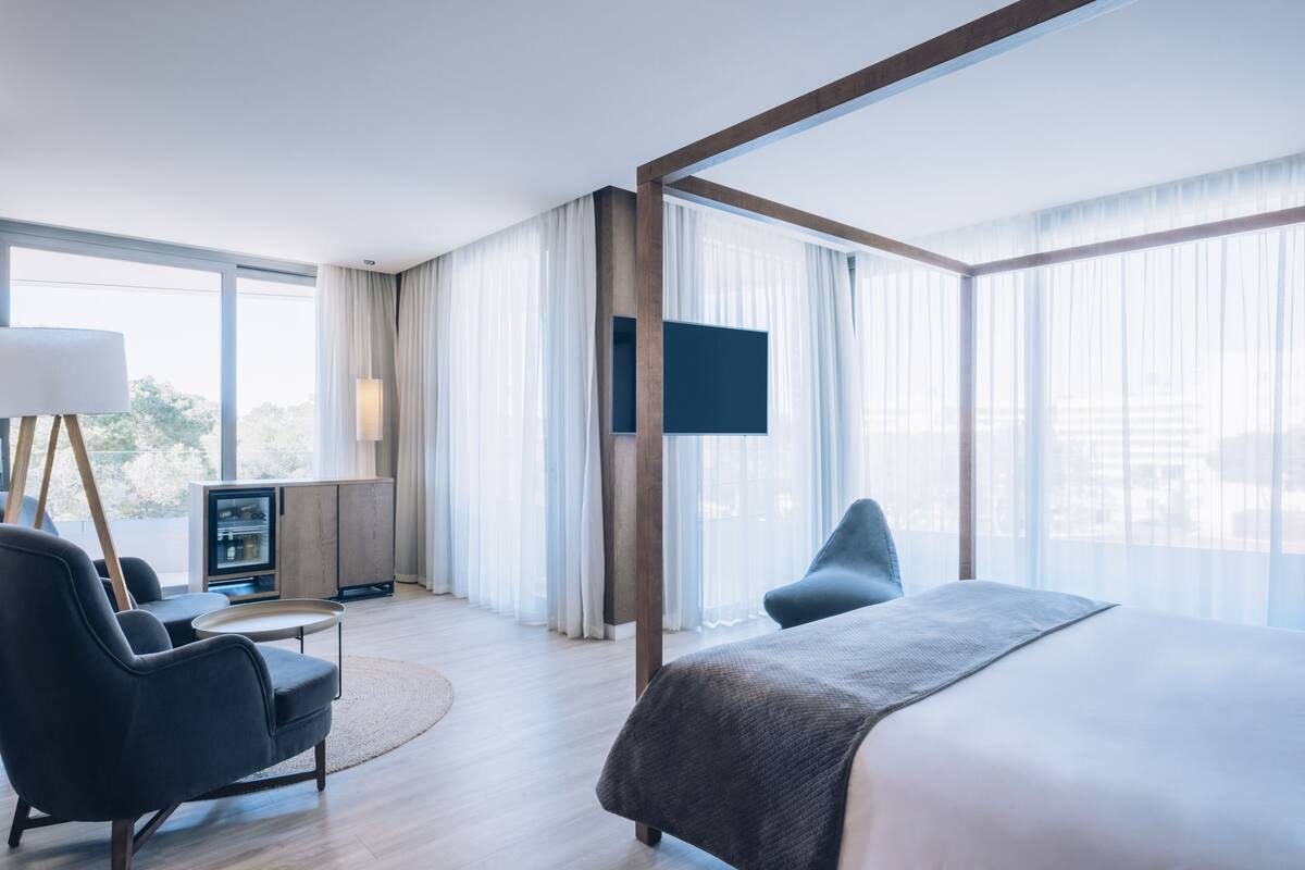 Ein modernes Hotelzimmer mit einem großen Bett, einem Schreibtisch, einem Sessel und einem Fernseher.