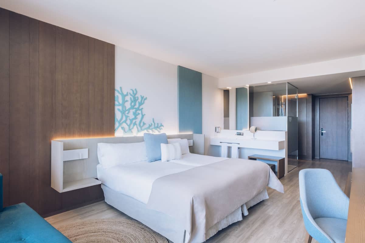 Ein modernes Hotelzimmer mit einem großen Bett, einem Schreibtisch, einem Stuhl, einem Spiegel und einem im Hintergrund sichtbaren Badezimmer.