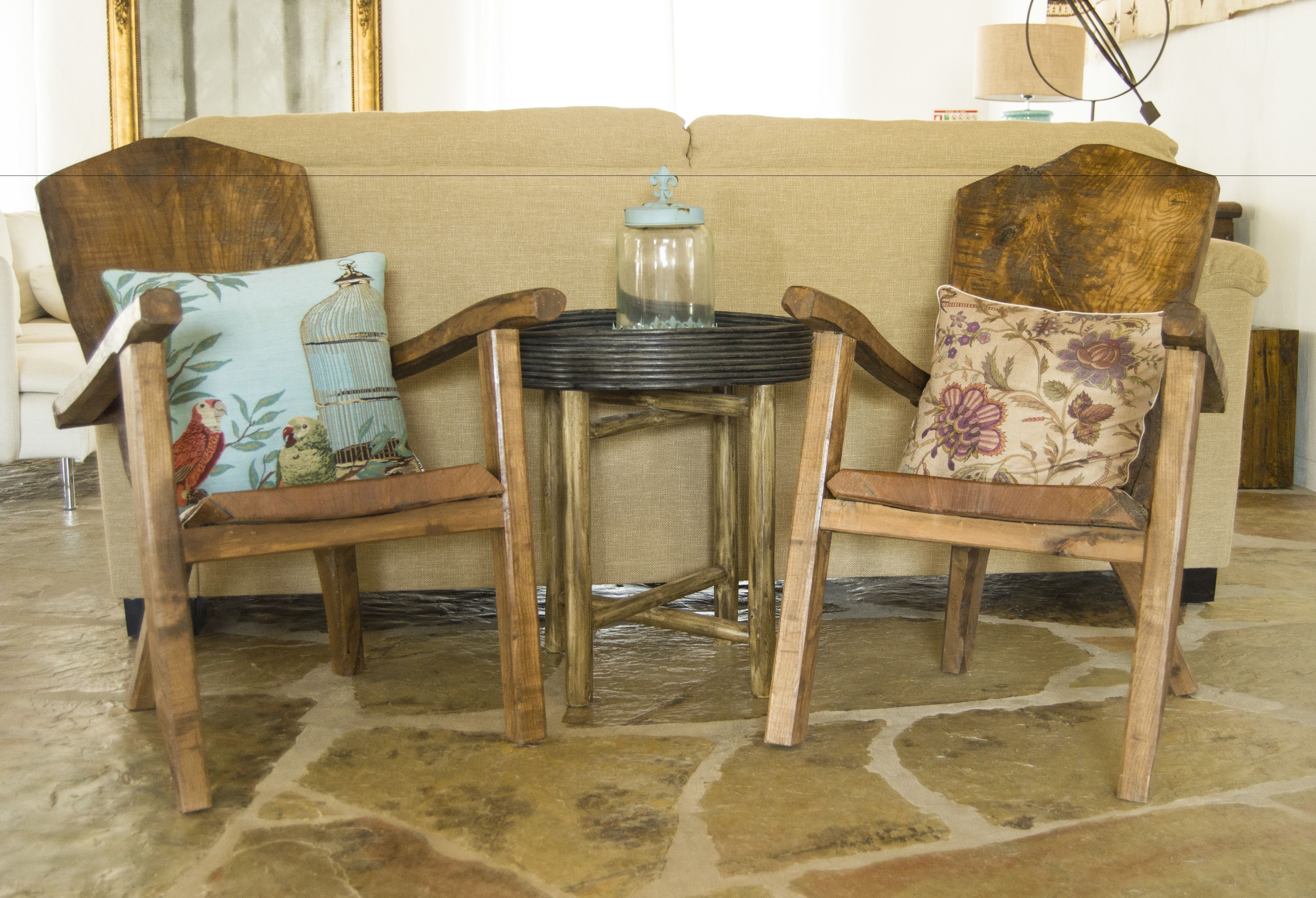 Dos sillas de madera, una con un cojín con diseño de pájaro y otra con un cojín floral, frente a un sofá beige.