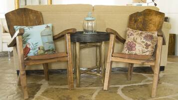 Dos sillas de madera, una con un cojín con diseño de pájaro y otra con un cojín floral, frente a un sofá beige.
