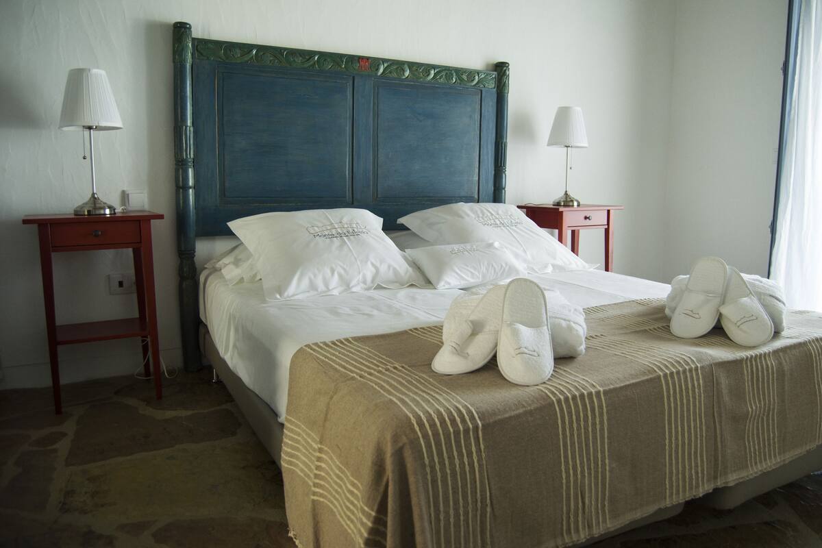 A neatly made bed with a headboard, two bedside tables with lamps, and a pair of slippers on the bed.