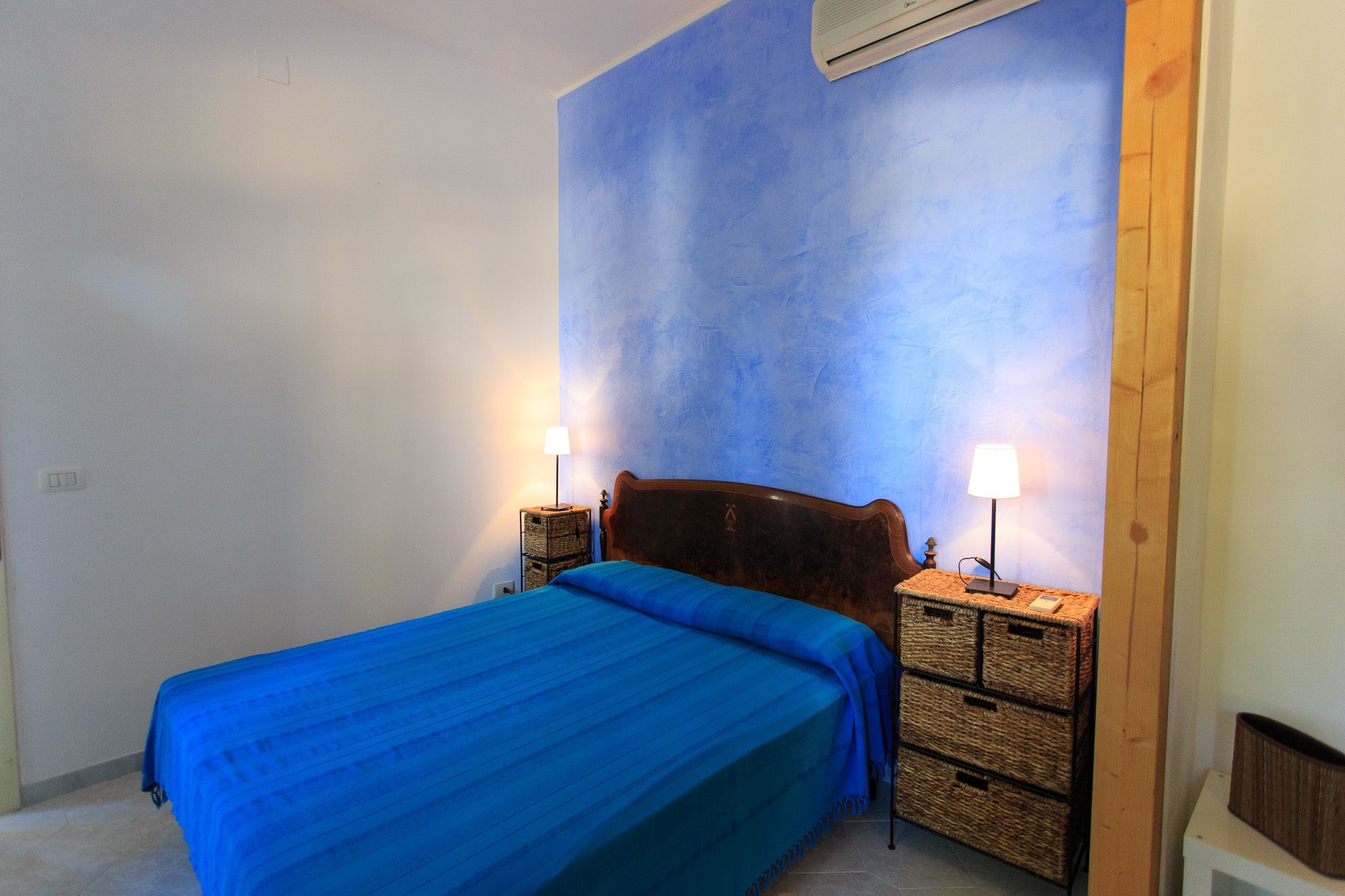 Quarto com cama, duas mesas de cabeceira e ar condicionado fixado na parede.