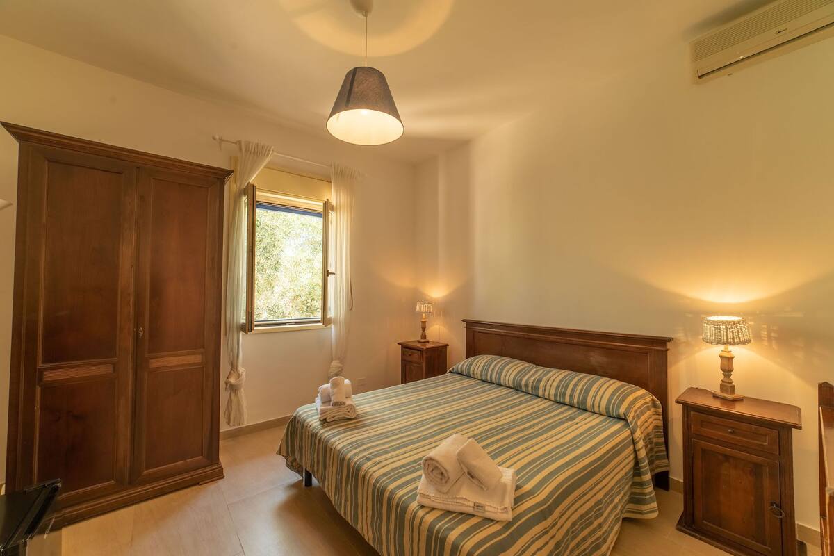 Un dormitorio con cama, mesitas de noche, ventana y armario.