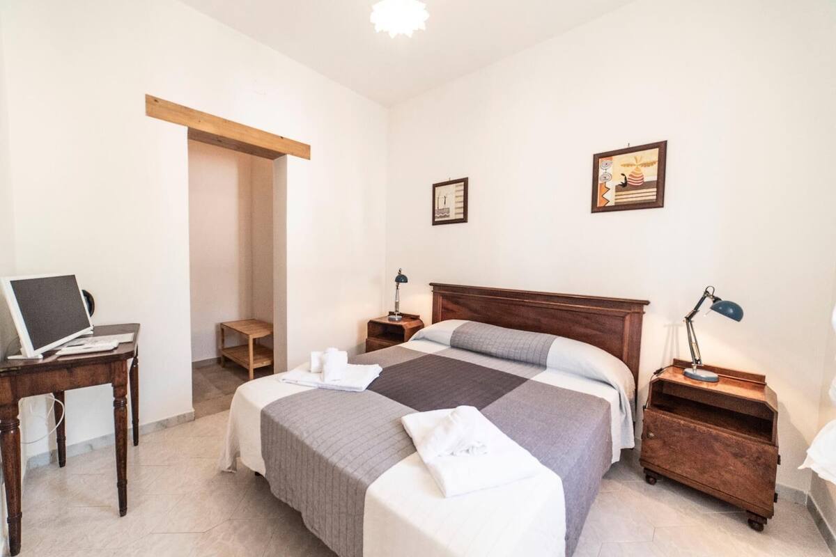 Habitación de hotel con cama, dos mesitas de noche, un escritorio con una computadora portátil y un armario de madera.