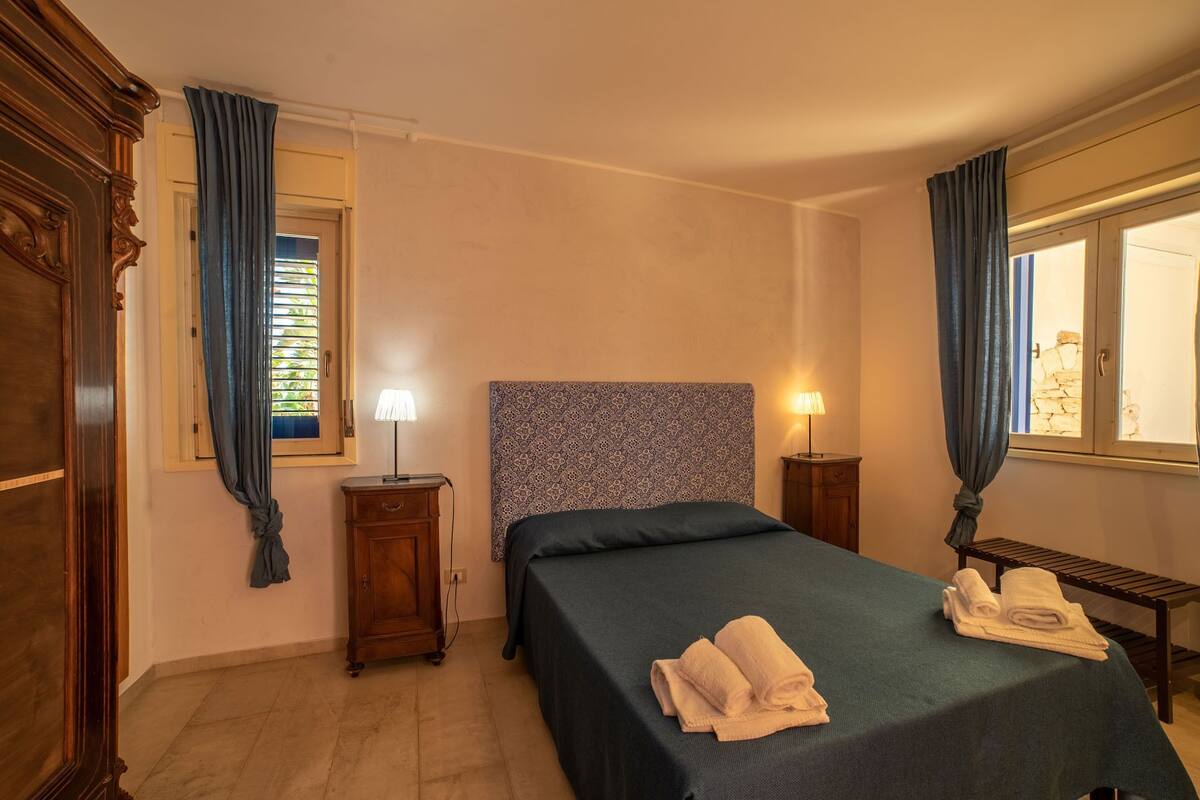 Un dormitorio con dos camas, un armario de madera, una mesita de noche con lámpara y una ventana con cortinas.