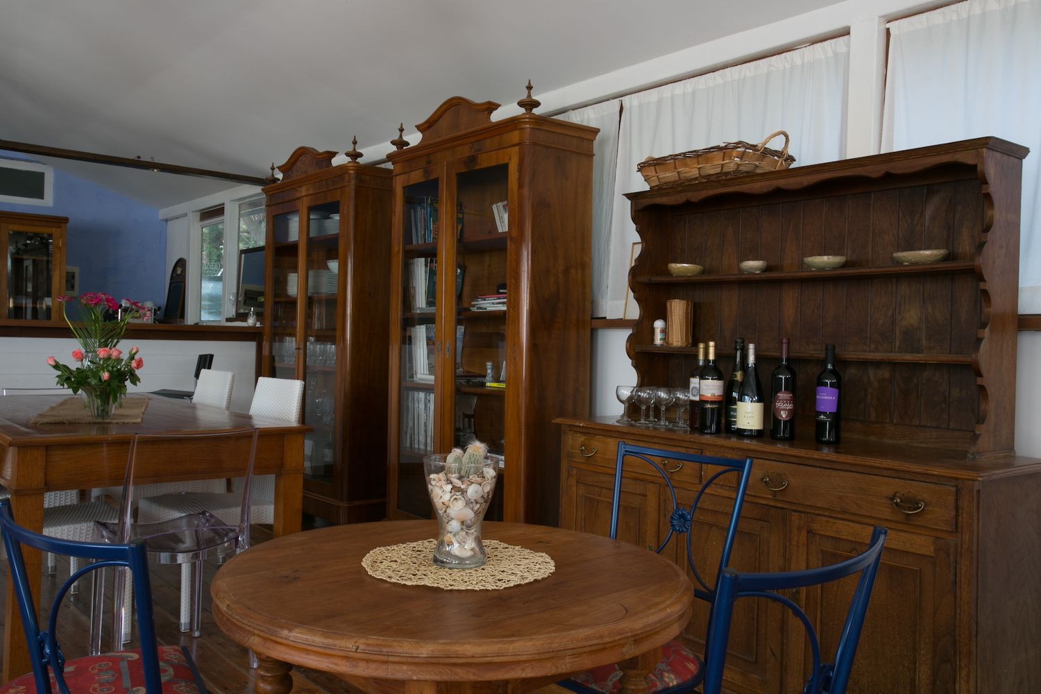Ein Essbereich mit einem Holztisch, Stühlen, einer Speisekammer mit Weinflaschen und einem Bücherregal.