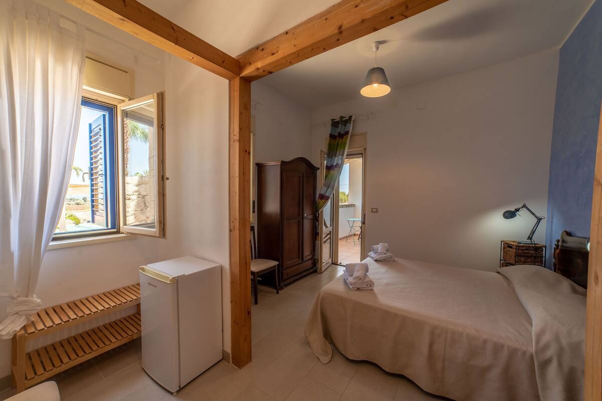 Un dormitorio con cama, un escritorio pequeño, un armario y una ventana con cortinas.
