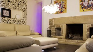 A modern living room with a beige sofa, a stone fireplace, and a colorful abstract painting. - Hotel Teratermal (Valdeavellano de Tera)