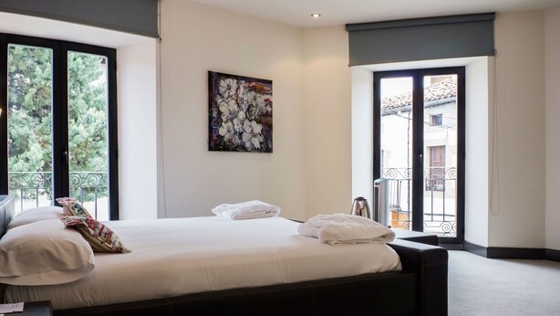 A bedroom with a large bed, a painting on the wall, and a balcony with a view. - Hotel Teratermal (Valdeavellano de Tera)