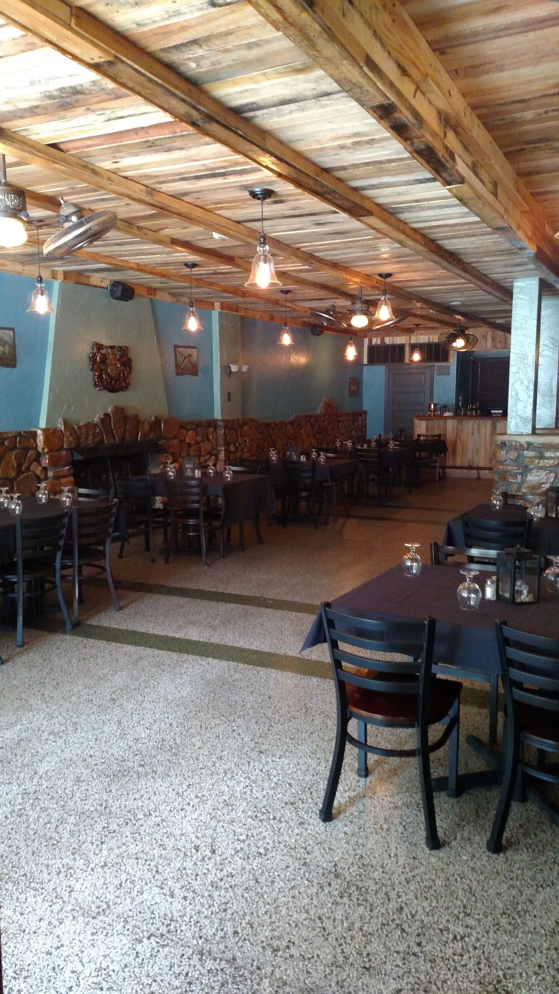 A rustic dining area with wooden beams, stone walls, and multiple tables and chairs.