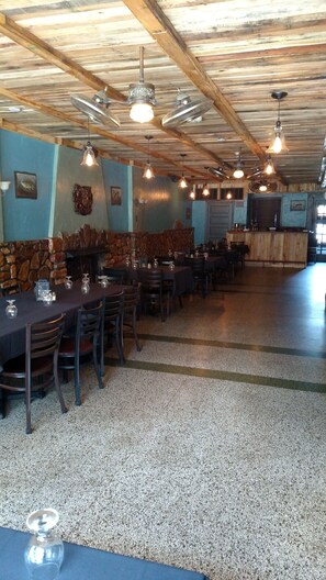 A restaurant with wooden beams, stone walls, and a stone fireplace. Tables are set with wine glasses and plates. - Ye Old English Inn (Hollister)