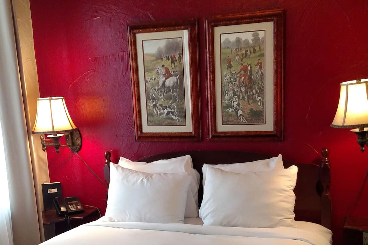 Een hotelkamer met een groot bed, twee nachtkastjes met lampen, en twee ingelijste foto’s aan de muur.