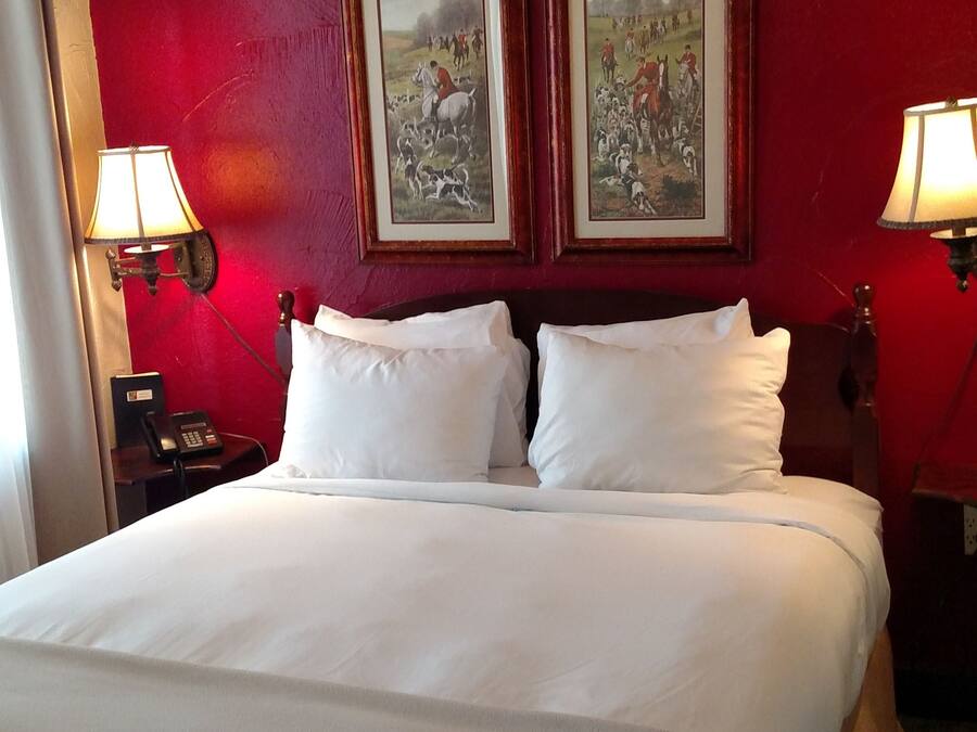 Quarto de hotel com uma cama grande, duas mesas de cabeceira com luminárias e duas imagens emolduradas na parede.