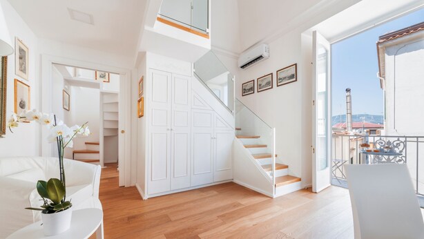 A spacious living area with a wooden floor, white furniture, a staircase, and a balcony with a view. - Palazzo Sassi (Meta)