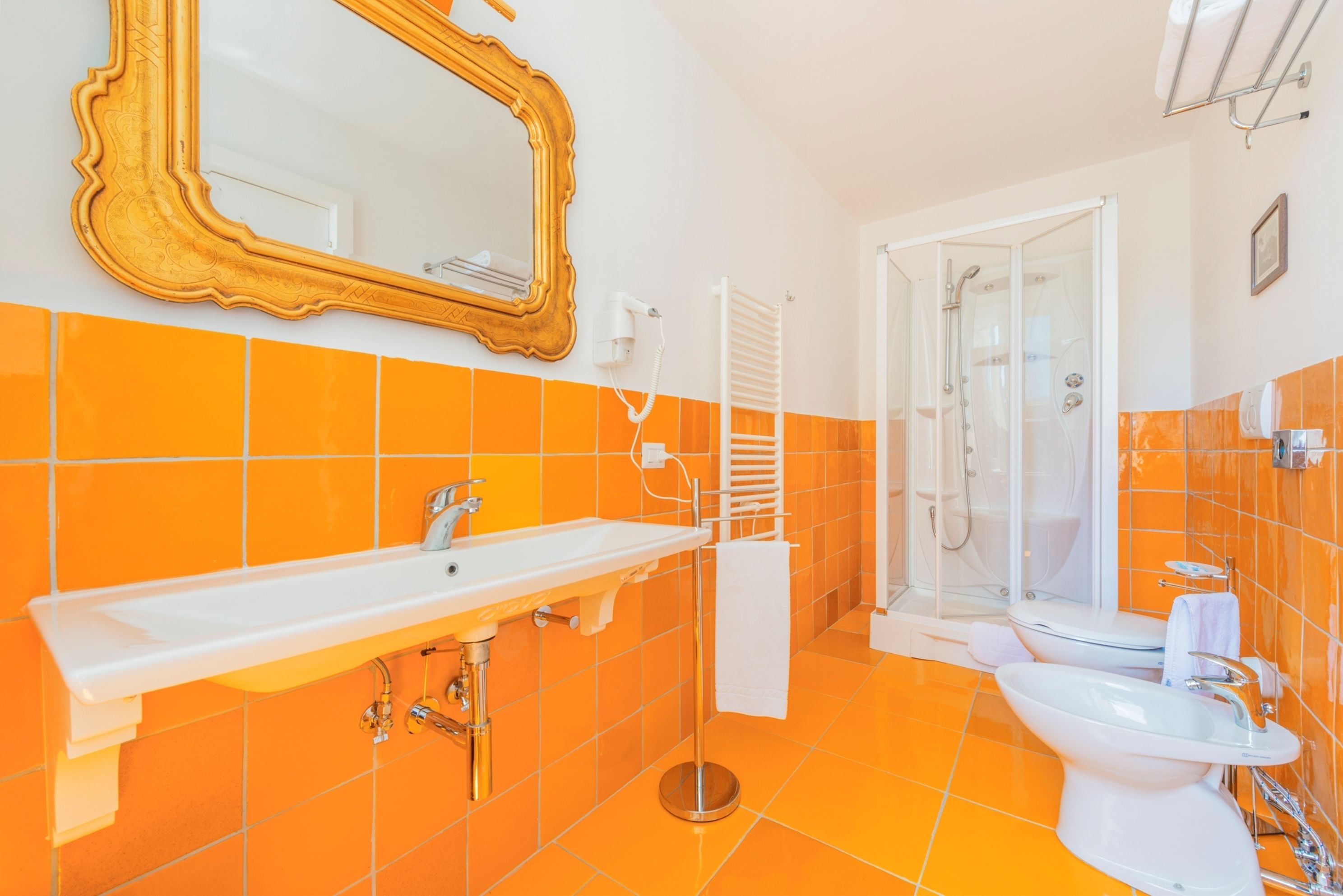 Une salle de bain avec des carreaux orange, un lavabo blanc, un miroir et un espace douche.