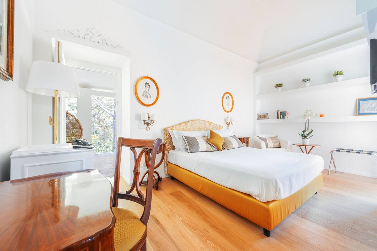 A bedroom with a bed, a wooden chair, a table, and a mirror.