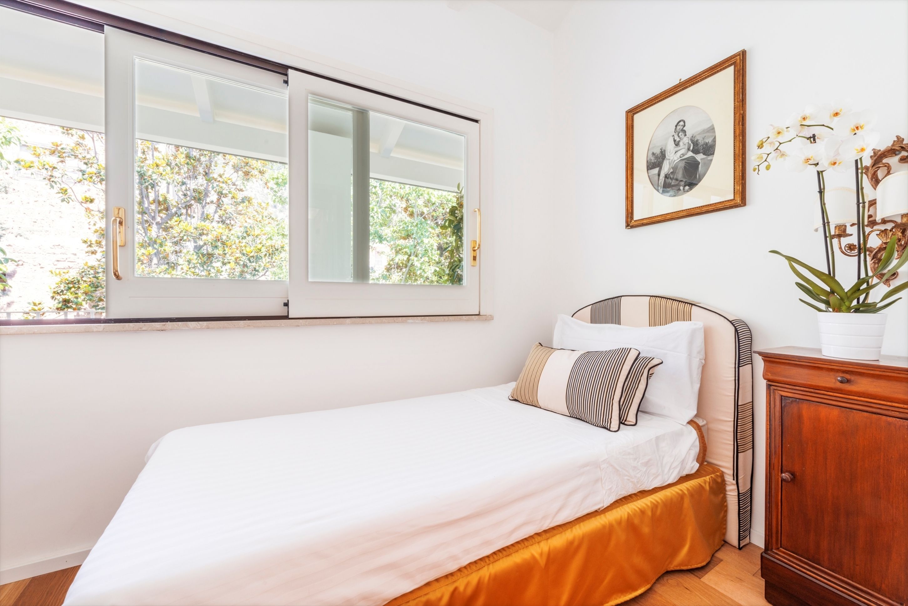 A bedroom with a bed, a window, a framed picture, and a cabinet.