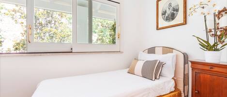 A bedroom with a bed, a window, a framed picture, and a cabinet.