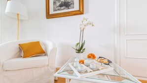 A modern living room with a white sofa, a glass coffee table with breakfast items, a potted orchid, and a framed picture on the wall. - Palazzo Sassi (Meta)