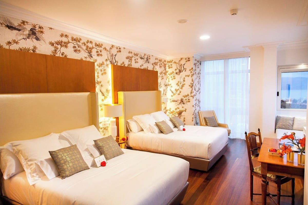 Quarto de hotel com duas camas, área de refeições e janelas amplas.