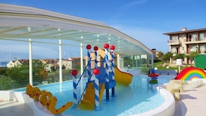 A pool area with slides and water features, surrounded by a glass canopy.