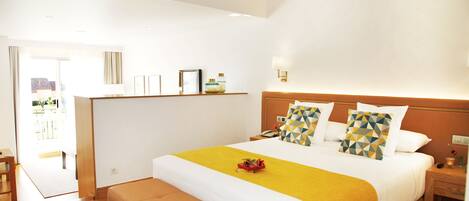 Habitación de hotel con una cama grande, una mesita de noche, un banco y vistas al exterior.