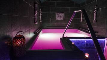 Un área de spa con una bañera de hidromasaje iluminada en rosa, adornos de pared de piedra y un farol.