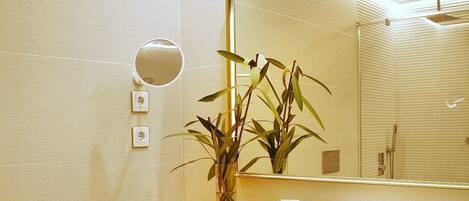 Een moderne badkamer met een grote spiegel, een wit wastafelmeubel en een plant.