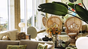 A spacious living room with a large window, a sofa, two rattan chairs, a coffee table, and a decorative vase with flowers.