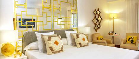 Habitación de hotel con una cama grande, dos sillones, una mesita y un espejo decorativo.