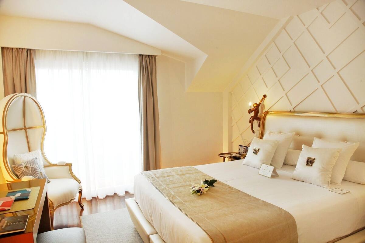 Quarto de hotel com uma cama grande, uma escrivaninha com cadeira, mesa de cabeceira e um objeto decorativo na parede.