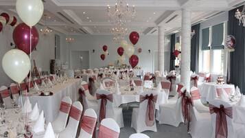 A banquet hall with round tables, white tablecloths, and chairs with red sashes.