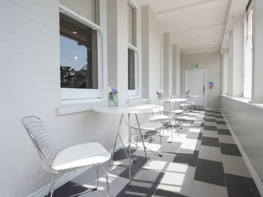 A corridor with white walls, checkered flooring, and a series of tables and chairs.